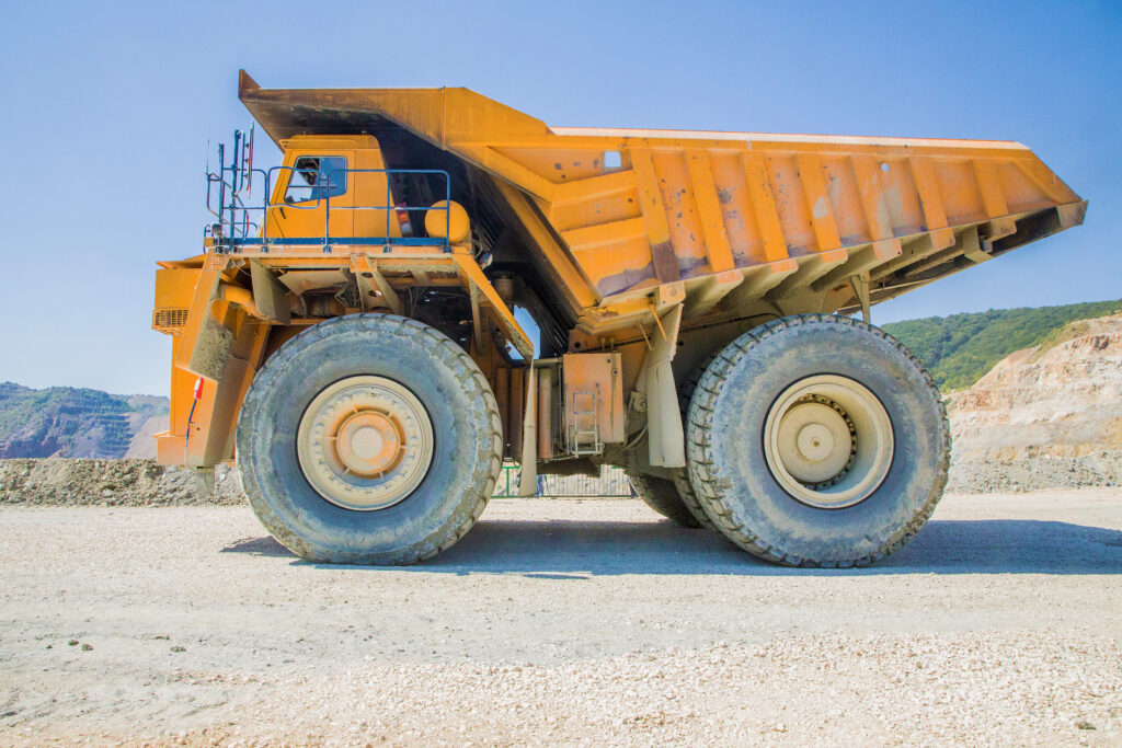 Side view of a large orange dump truck in a mining site, emphasizing its massive tires and rugged construction, relevant to obtaining a QLD truck licence.