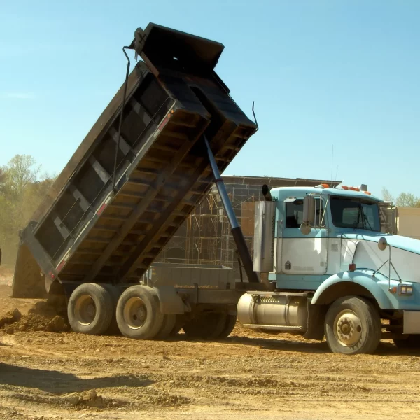 Dump truck unloading dirt on a construction site, illustrating the practical application of skills for obtaining a dump truck licence in Queensland.